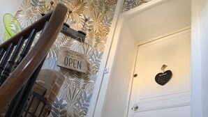 A staircase with a wooden handrail, a 'WELCOME' sign, a 'OPEN' sign, and a heart-shaped plaque on a white door.