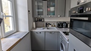 A compact kitchen with grey cabinets, a washing machine, a microwave, and a sink.