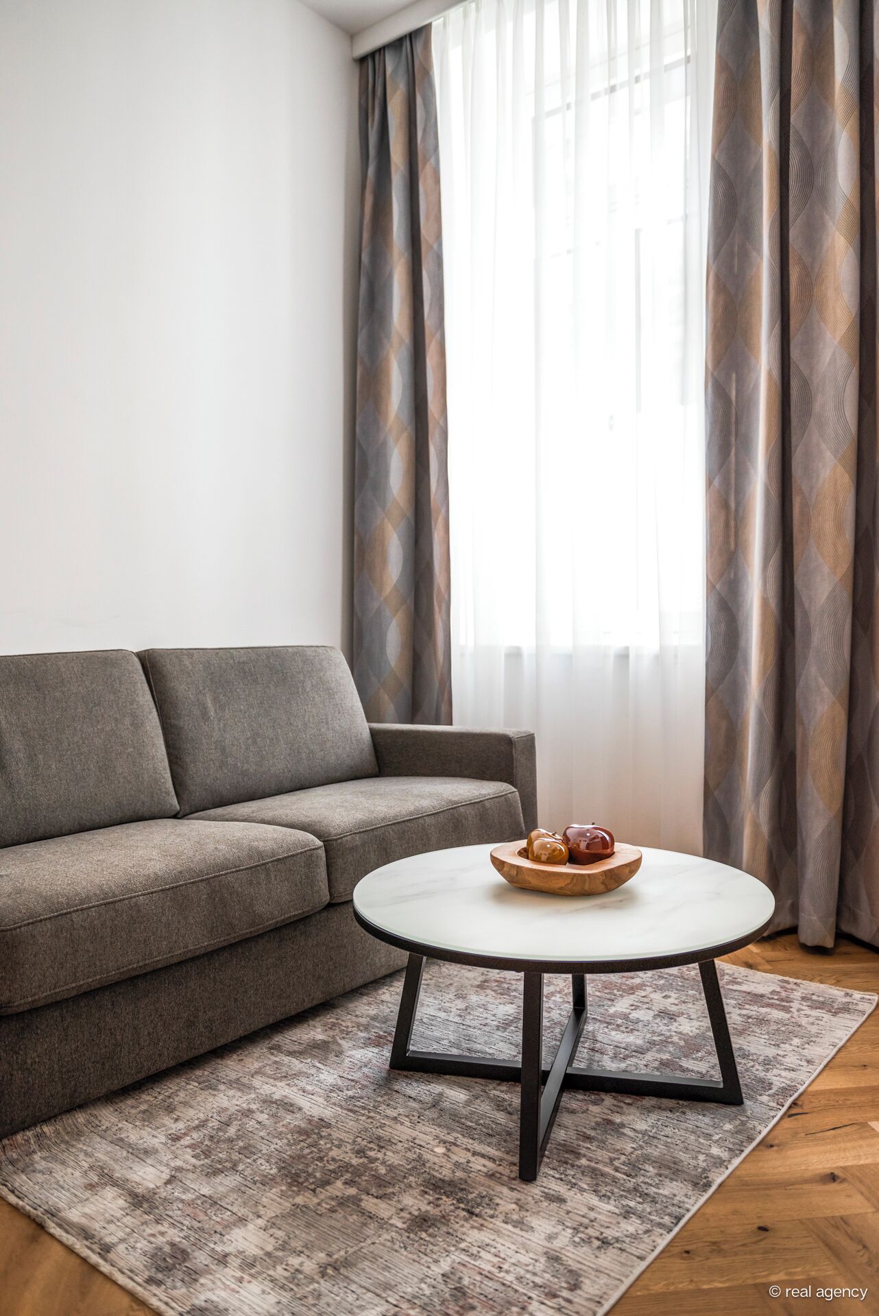 A living room with a grey sofa, a round coffee table with a wooden base, and a patterned rug.