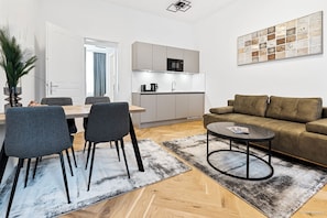 A modern living room with a sofa, coffee table, and dining area with chairs. - easy-flat Rokitanskygasse - Apartments near Tram 43 to City Center (Vienna)
