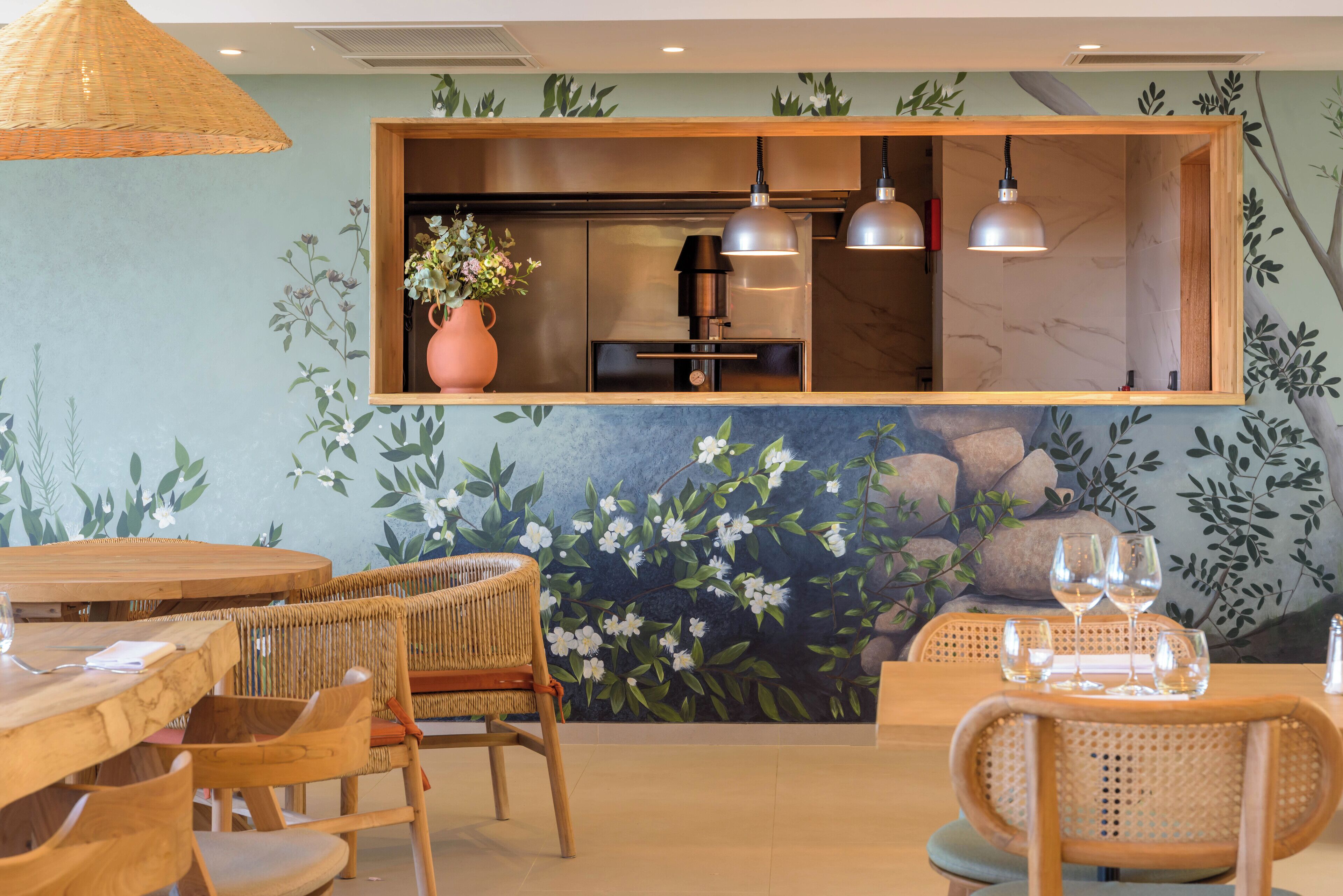A restaurant interior with wooden furniture, a mural with flowers and leaves, and pendant lights.