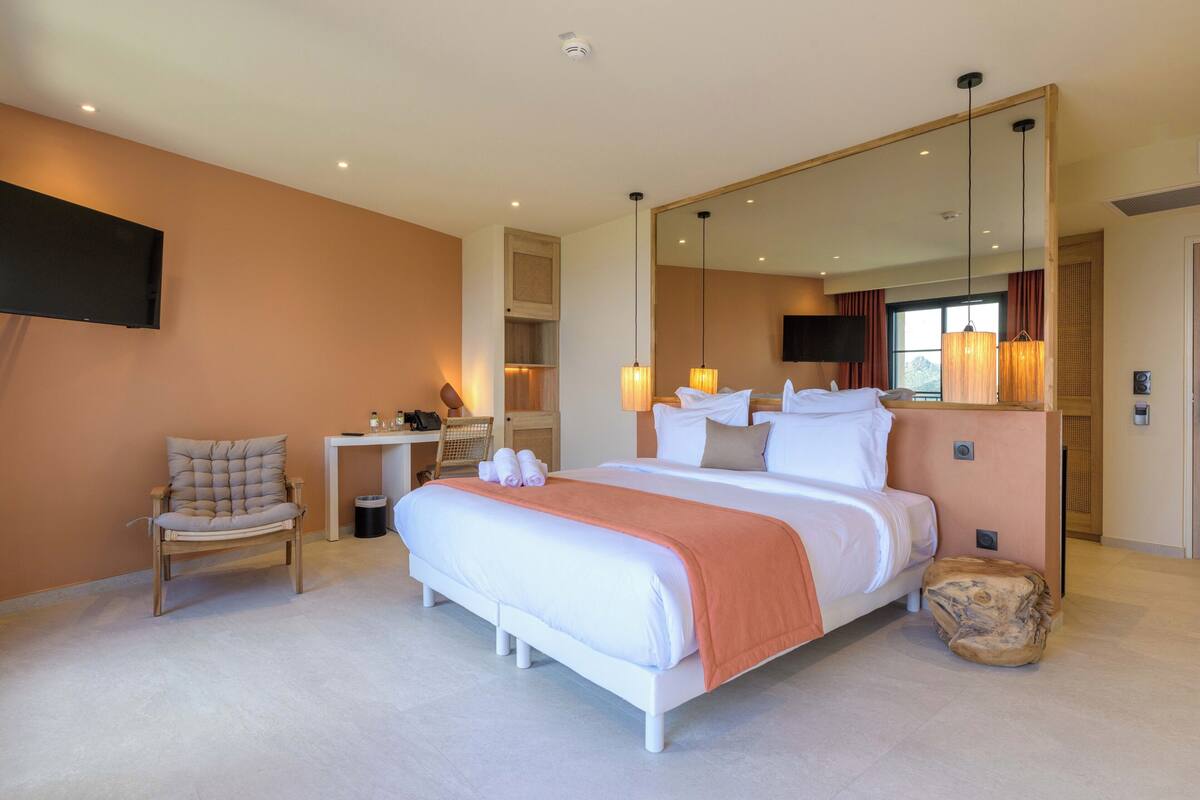 A modern hotel room with a large bed, a chair, a desk, and a mirror.