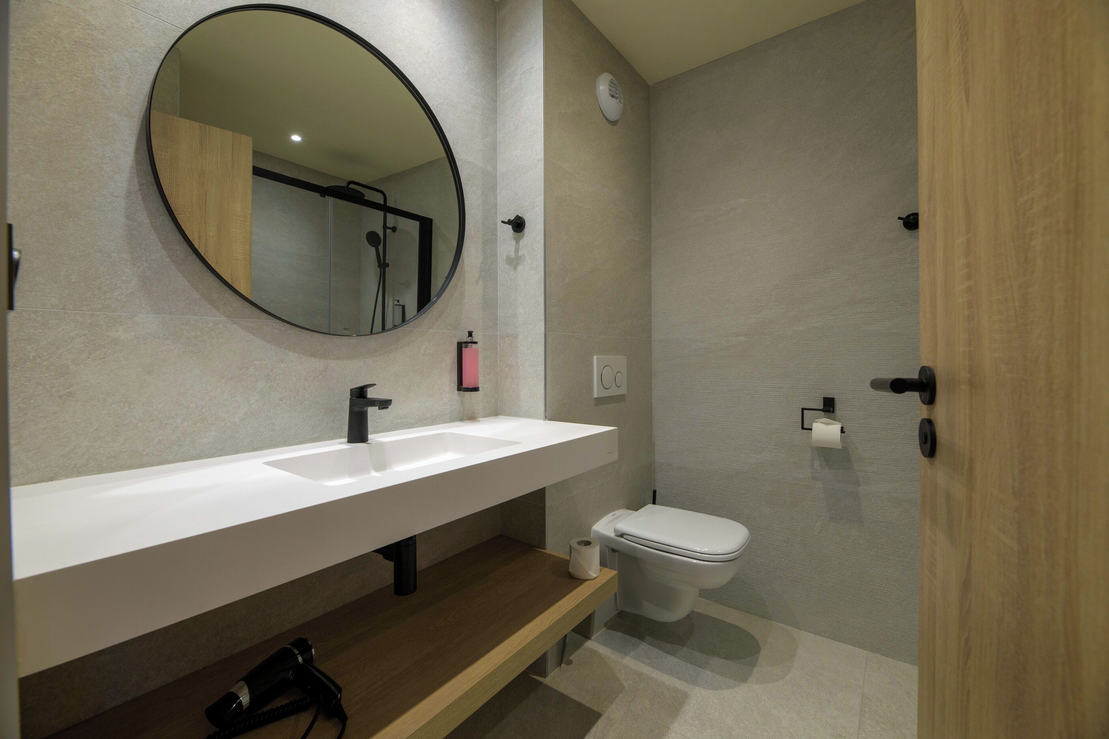 Un baño moderno con espejo redondo, lavamanos blanco y un inodoro.