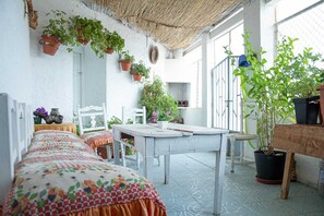 A room with a long table, chairs, hanging plants, and a thatched ceiling. - Cueva Navarro      . (Gorafe)