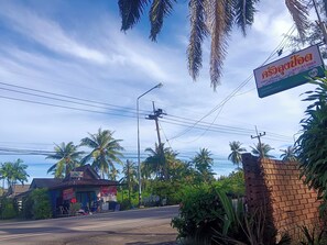 A street view with a small building that appears to be a shop or restaurant, surrounded by palm trees and a clear sky.