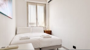 A minimalist bedroom with a bed, bedside table, and a window with sheer curtains. - Italianway Easy - Toscana 17 (Milan)