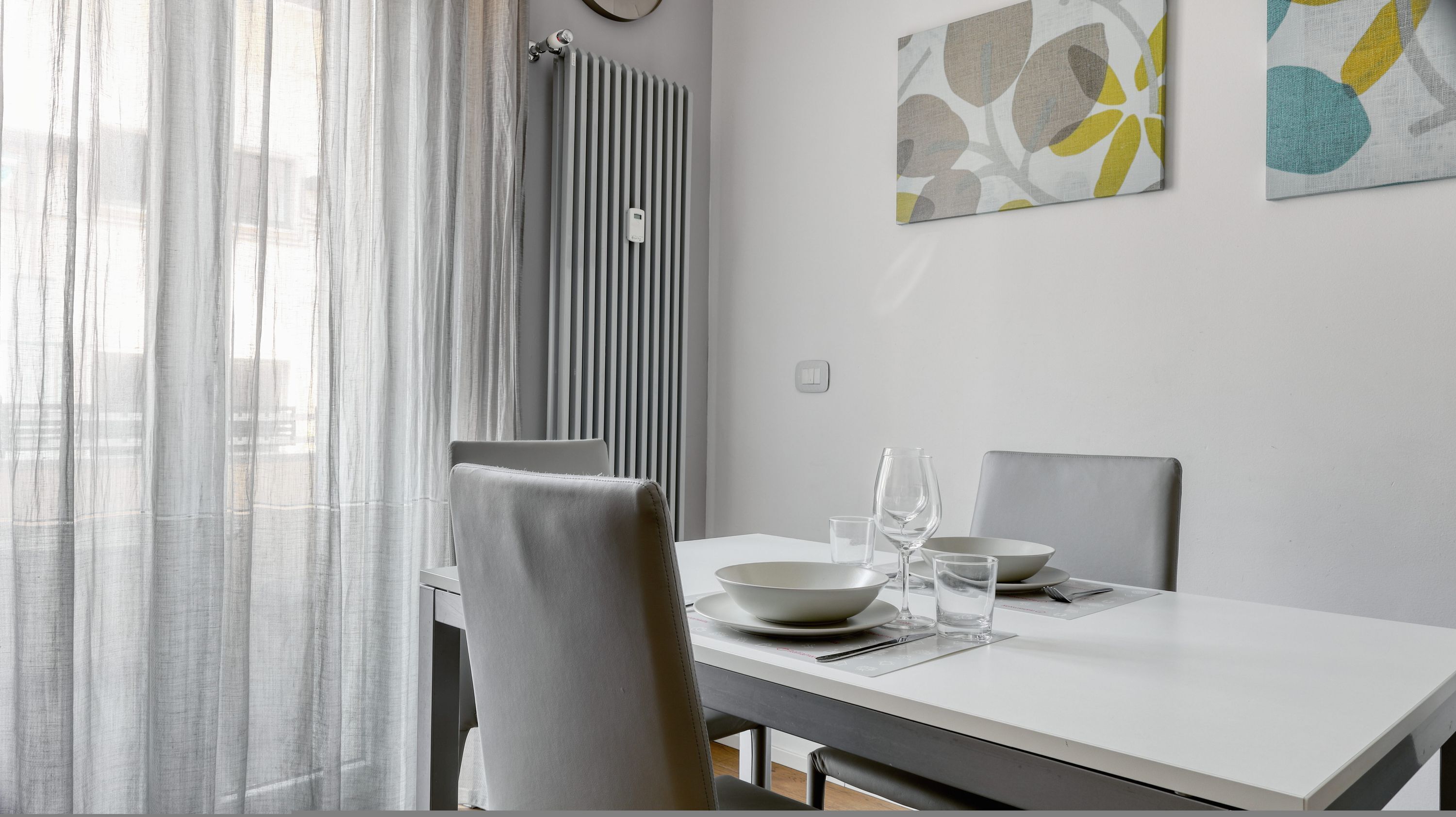 A modern dining area with a white table, grey chairs, and a sheer curtain.