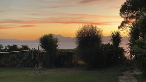Un chemin pavé mène à une zone herbeuse où se trouve un lampadaire, et d’où l’on peut admirer le coucher de soleil sur la mer.