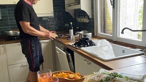 Une cuisine où une personne prépare des aliments, avec un évier, une fenêtre et un plan de travail sur lequel se trouvent divers objets.