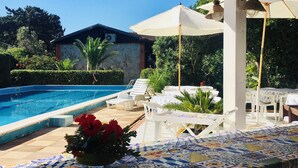 Un espace aménagé au bord de la piscine, avec une terrasse carrelée, des chaises longues et une table recouverte d’une nappe à motifs.
