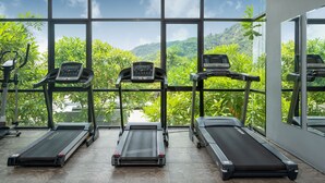 Un gimnasio con cintas de correr y elípticas, amplias ventanas que ofrecen vistas a exuberante vegetación y colinas.
