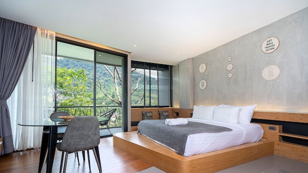 Un dormitorio moderno con una cama grande, una mesa de comedor y vistas a zonas verdes por la ventana.