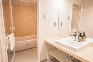 A modern bathroom with a bathtub, a large mirror, and two sinks. - WAYFARER Gojo (Kyoto)