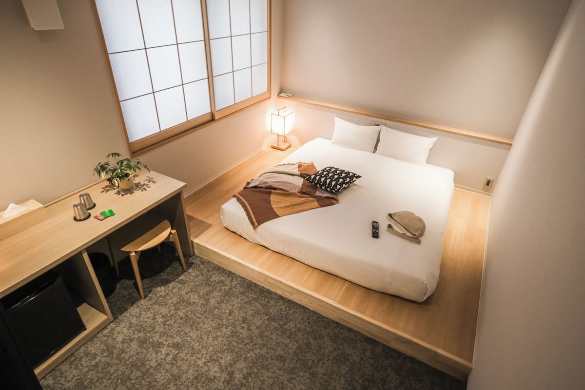 A compact hotel room with a bed, bedside table, lamp, and a small desk with a chair.
