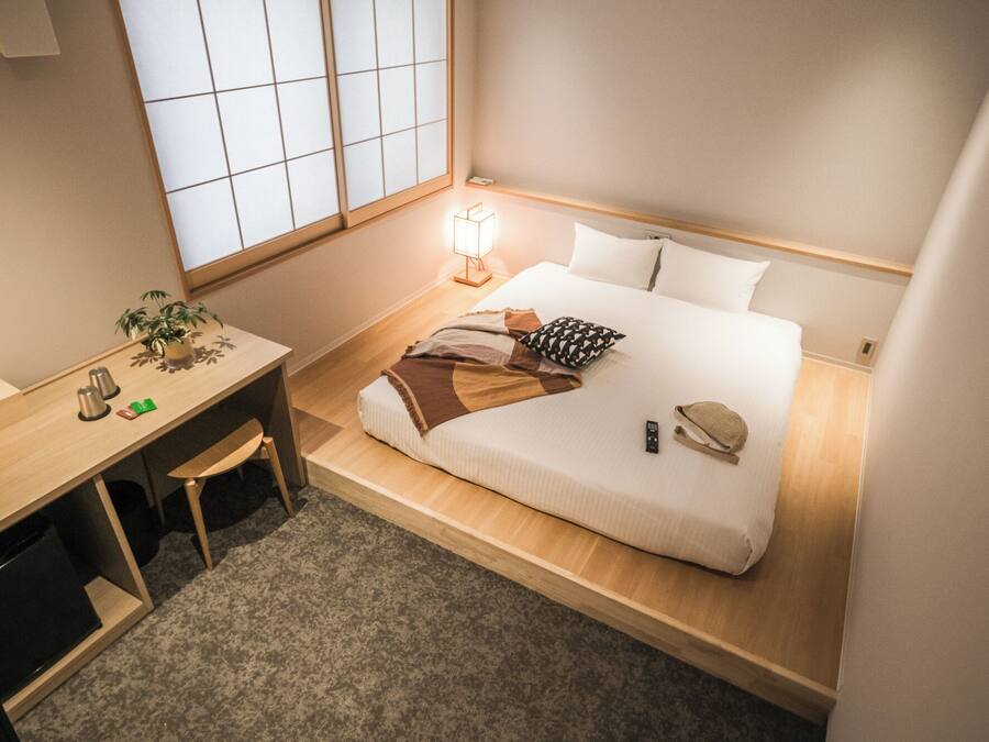 A compact hotel room with a bed, bedside table, lamp, and a small desk with a chair.