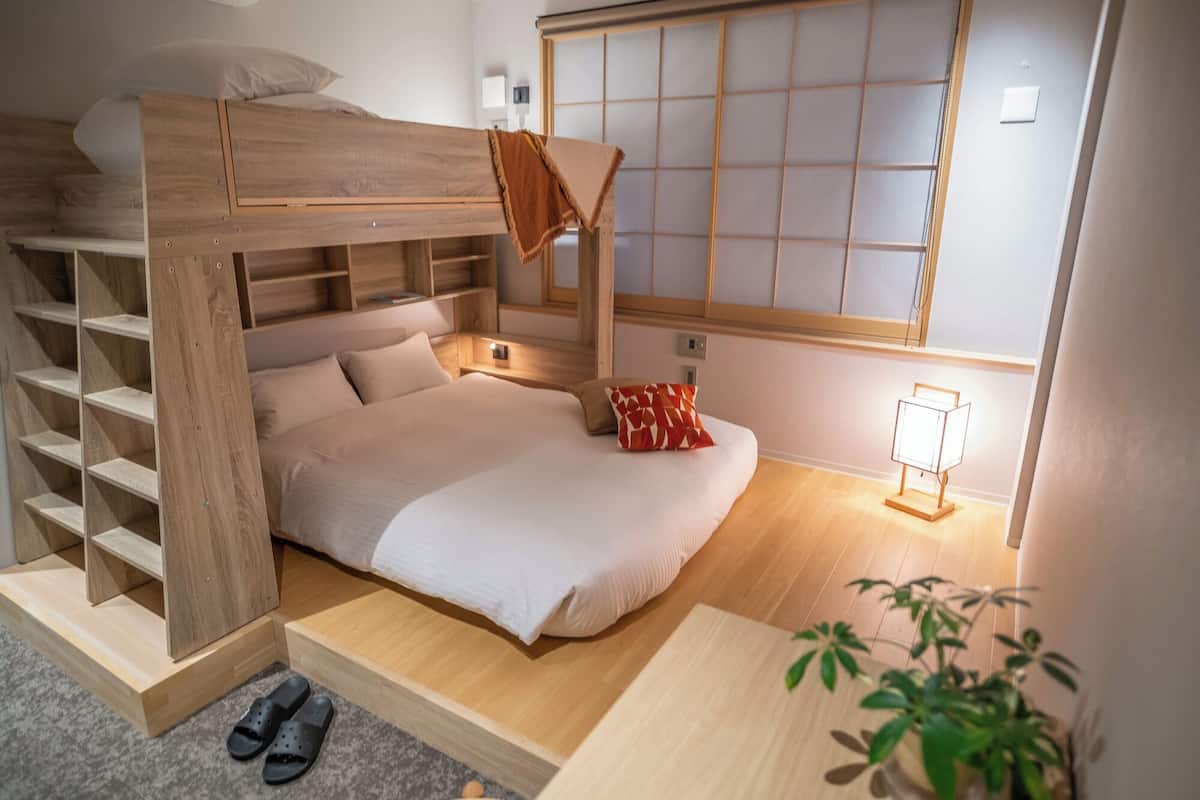 A bunk bed with wooden shelves, a bedside table, a lamp, and a plant.