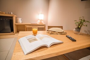 A wooden table with a book, a glass of orange juice, a remote control, and a plant. - WAYFARER Gojo (Kyoto)
