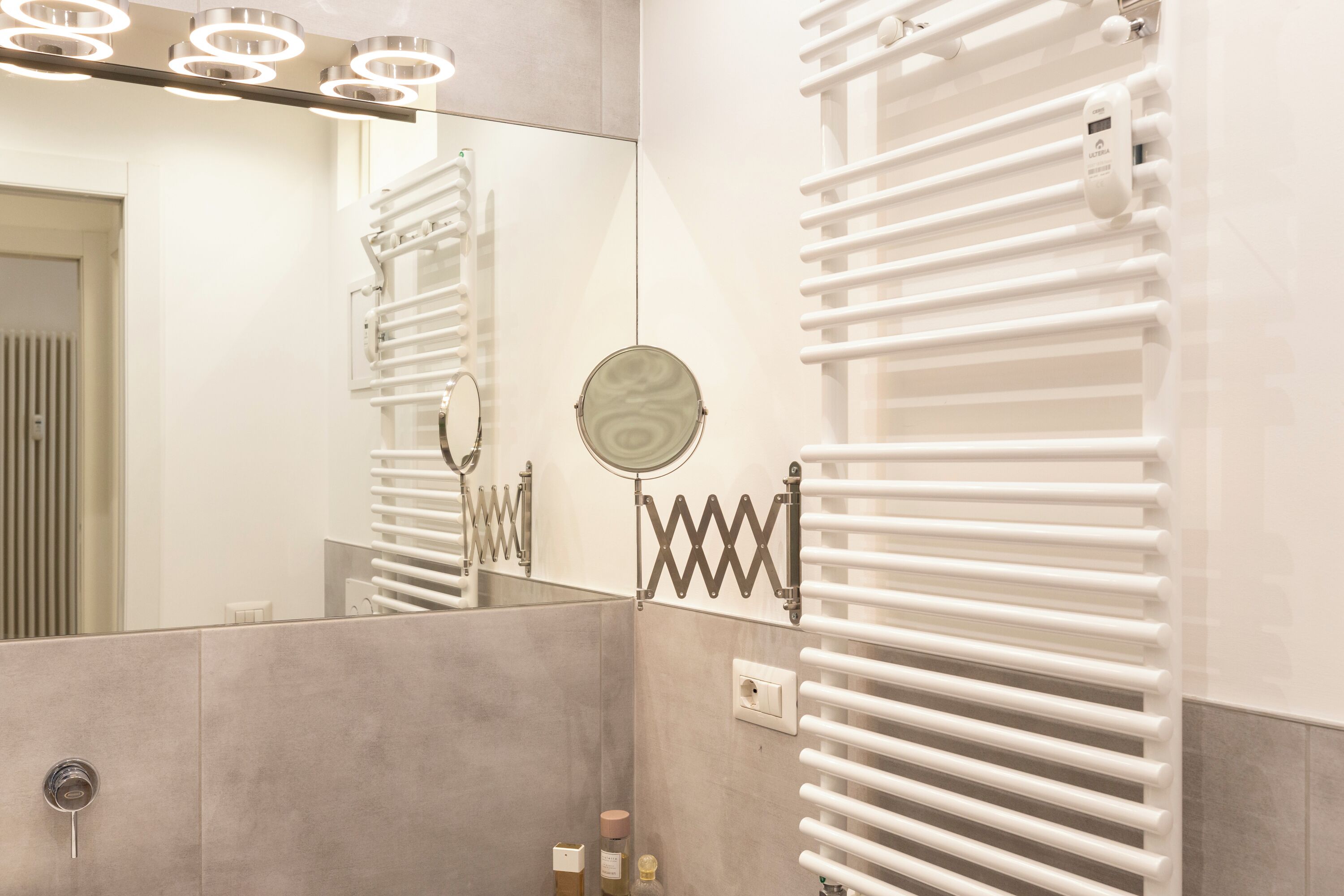 A modern bathroom with a large mirror, a towel rack, and a built-in heater.