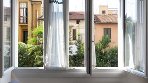A window with a view of a residential area, including buildings and greenery. - notaMi - Monte Ceneri Suite (Milan)
