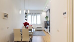 A modern kitchen with white cabinets, a built-in oven, and a microwave. There is a dining area with a table and chairs, and a window with curtains. - notaMi - Monte Ceneri Suite (Milan)