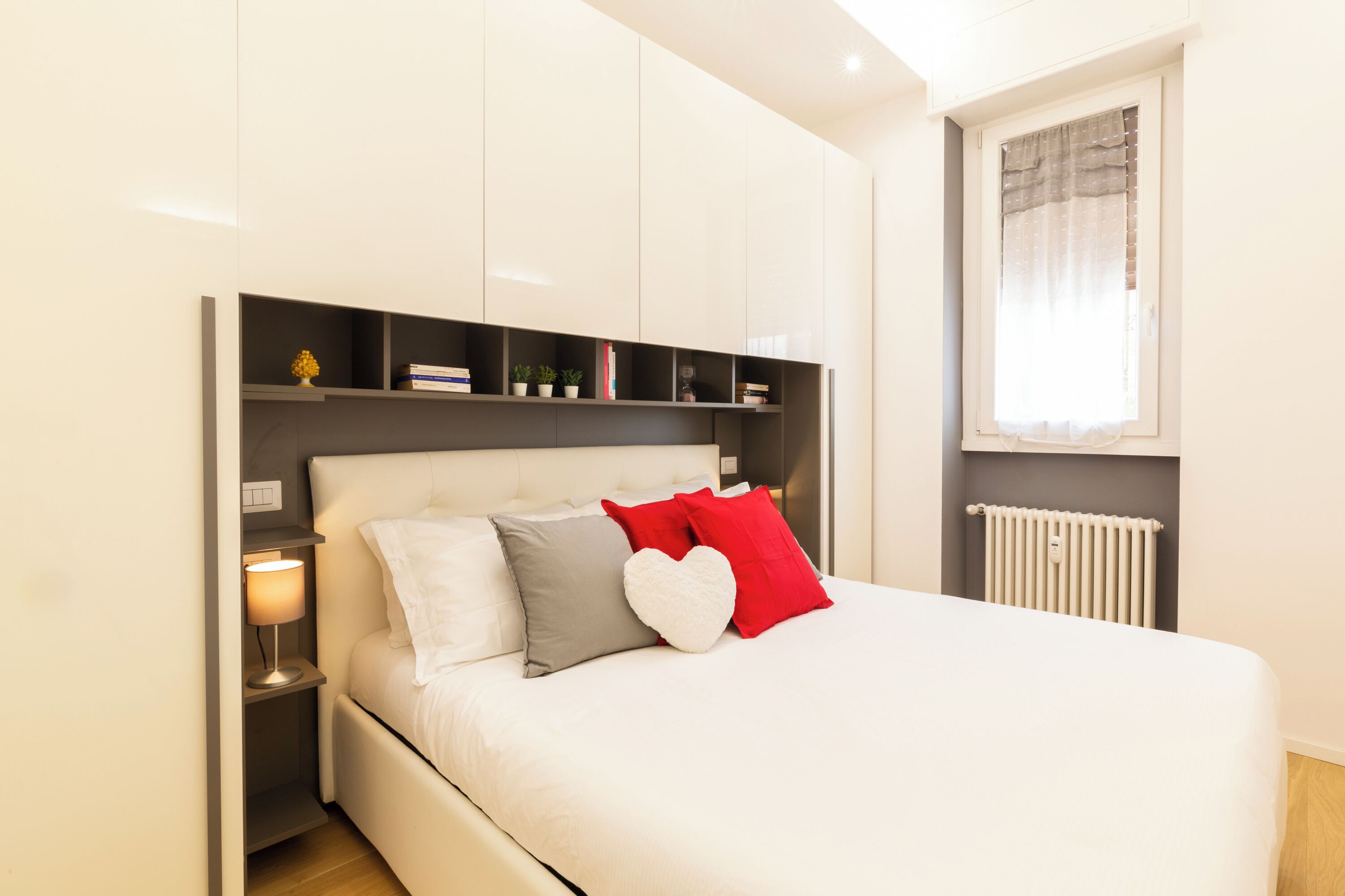 A bedroom with a bed, bedside tables, a nightstand, a window with curtains, and built-in shelving.