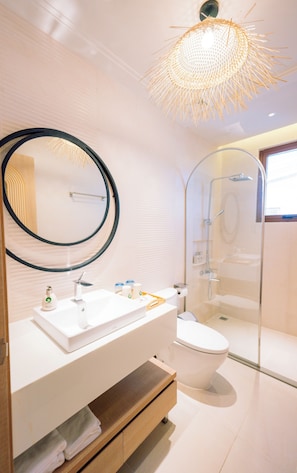 A modern bathroom with a white sink, toilet, and shower. There is a large mirror above the sink and a unique light fixture above the shower. - Lotus Home Corner & Rooftop (Phu Quoc)