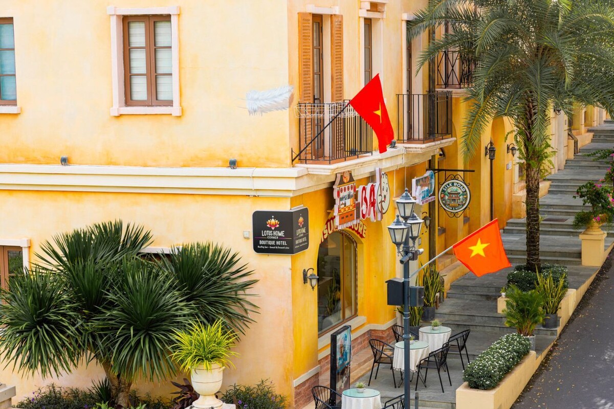 Un hotel con fachada amarilla, mesas al aire libre y banderas.