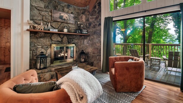 A cozy living room with a stone fireplace, a comfortable seating area, and a large sliding glass door leading to an outdoor deck.