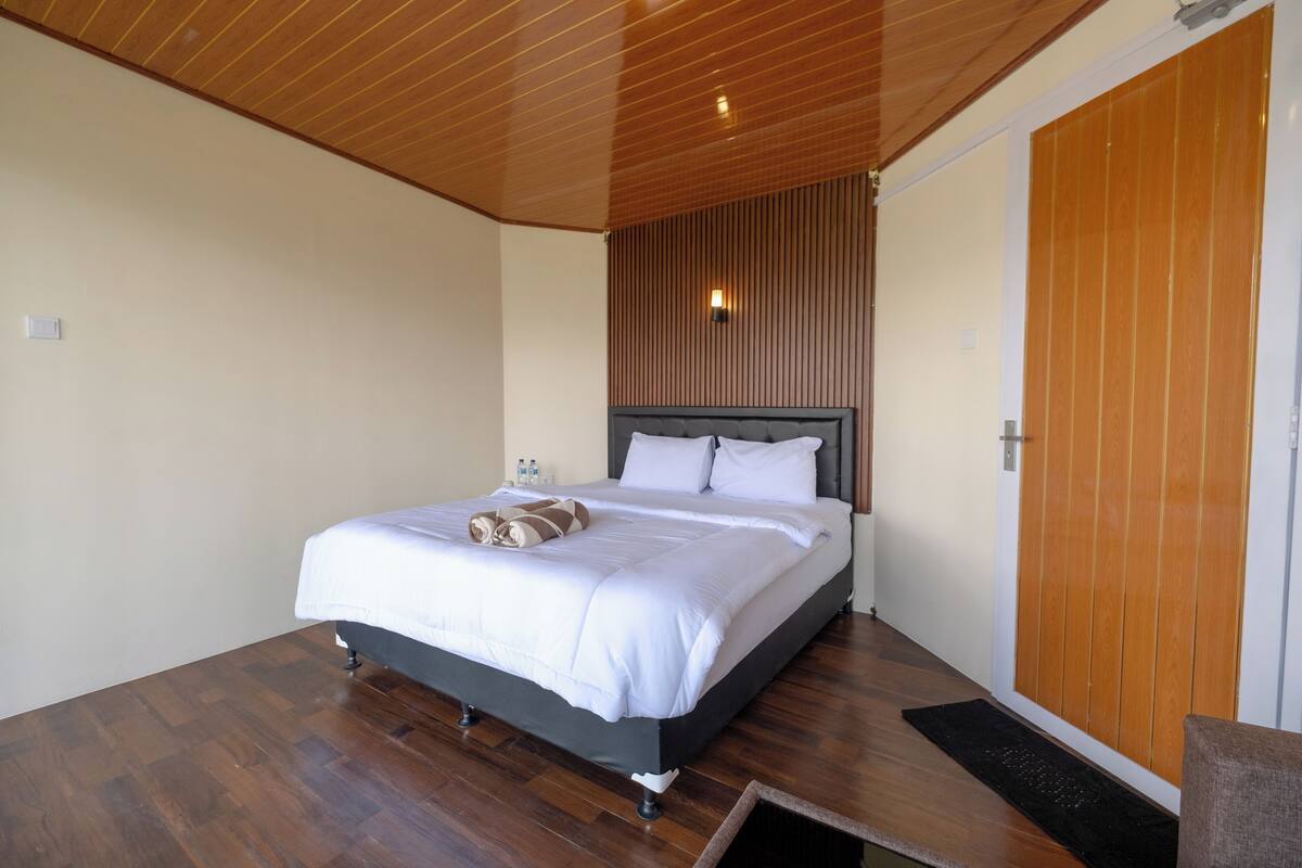 Una cama bien hecha con sábanas blancas y una toalla marrón, suelo de madera y techo de madera.