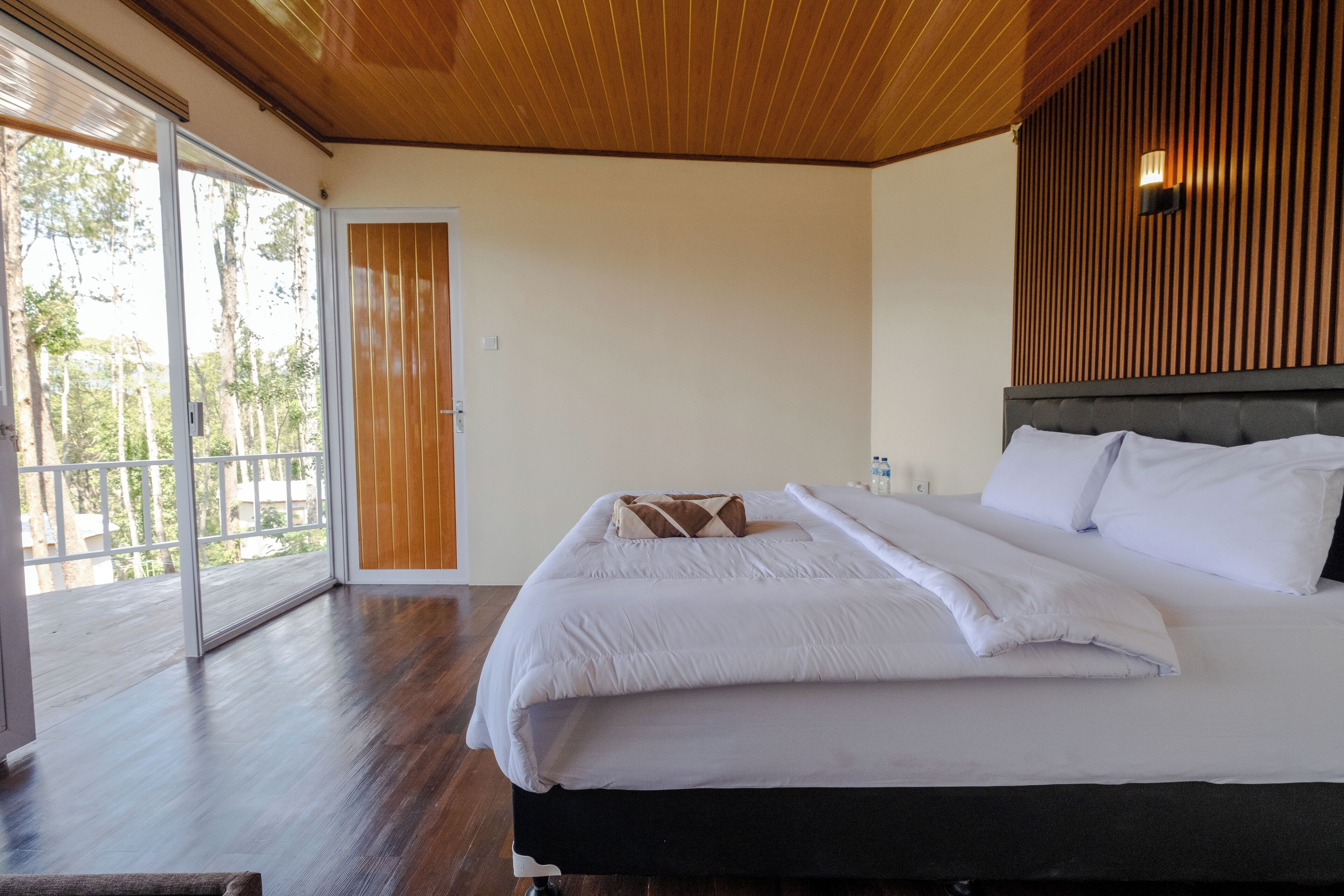 A bedroom with a large bed, wooden ceiling, and a sliding glass door leading to an outdoor area.