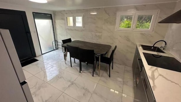 Een moderne keuken met een marmeren aanrecht, een eethoek met een tafel en stoelen, en een raam met uitzicht op groen.