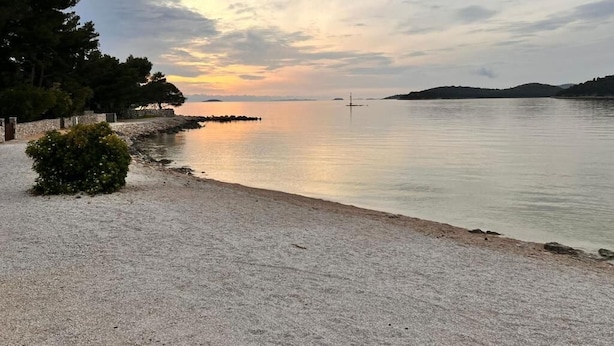 A beach with a calm sea, a stone wall, and trees. - Holiday house Mia (Rogoznica)
