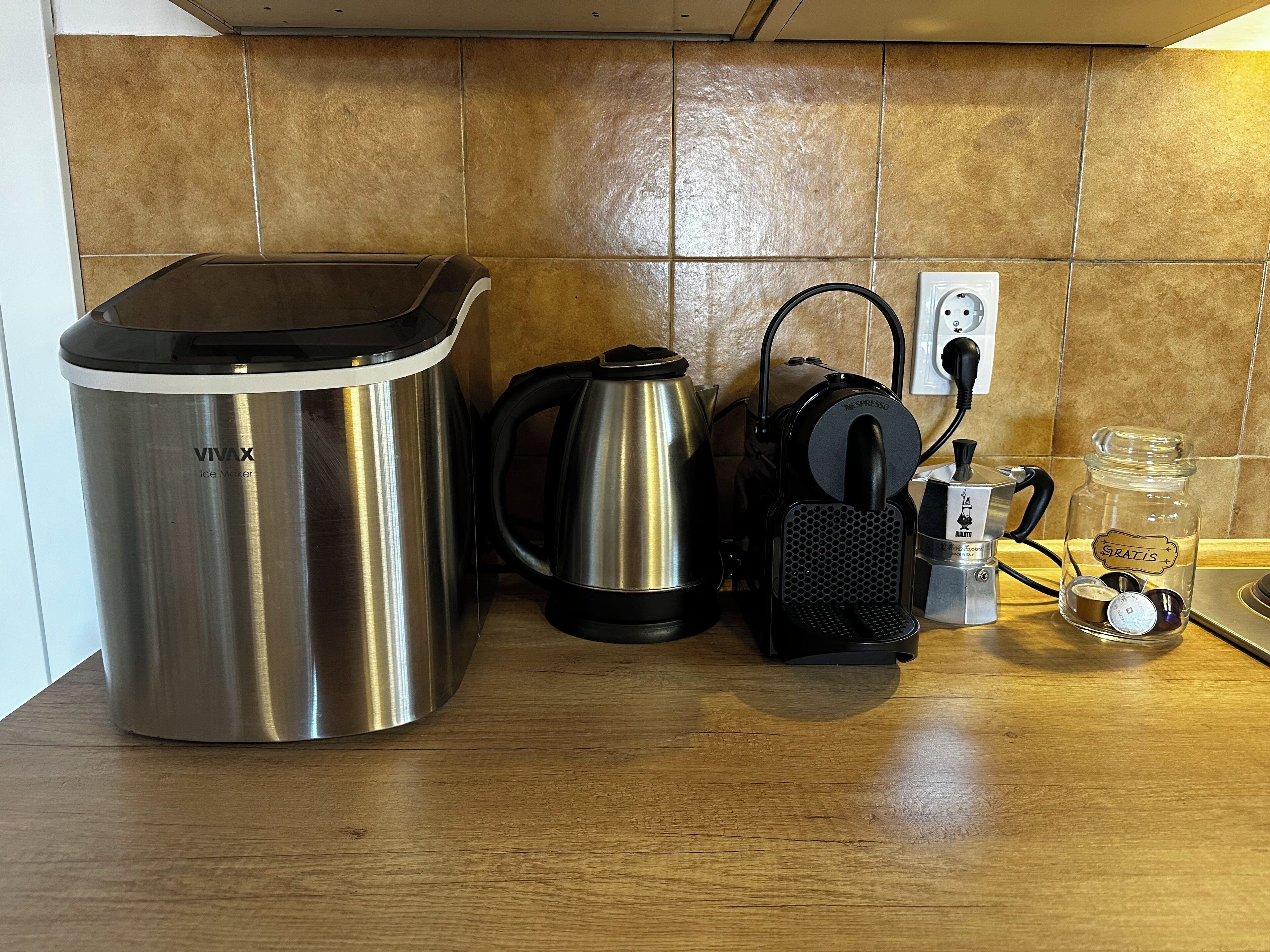 Un comptoir de cuisine avec un appareil à glaçons en acier inoxydable, une machine à café noire, une machine Nespresso et un bocal étiqueté « Gratuit ».