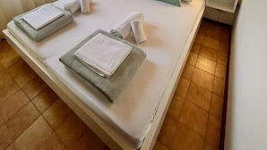 A neatly made bed with pillows and folded towels, wooden ceiling, and two bedside lamps. - Holiday house Mia (Rogoznica)