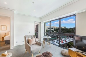 Un salon moderne avec une grande fenêtre, un canapé, un téléviseur et une petite table.