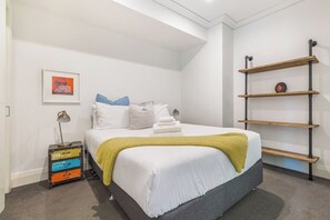 Une chambre d’hôtel avec un lit, une étagère, un tableau encadré et une lampe de chevet.