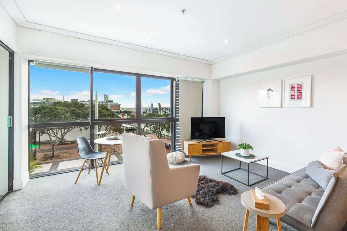 A modern living room with a large window, a sofa, a chair, a TV, and a small table.