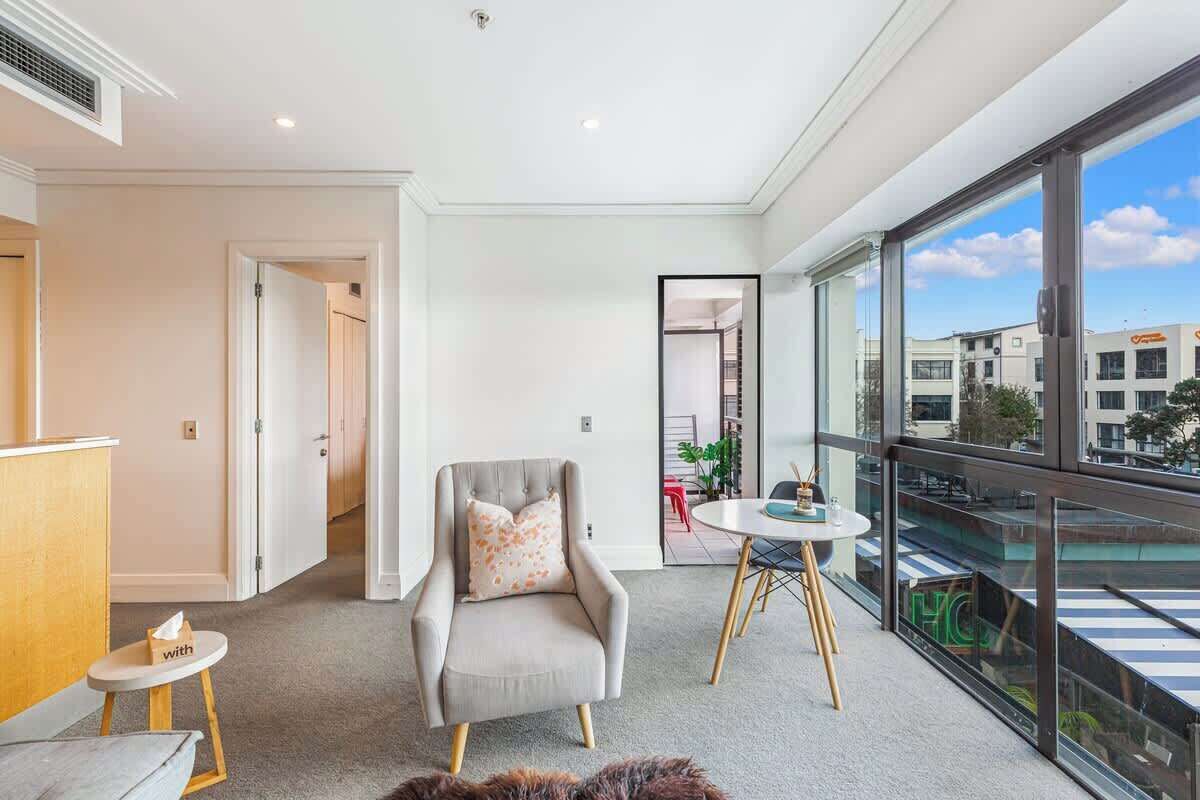 A modern hotel room with a balcony, a seating area with a small table, and a large window offering a city view.