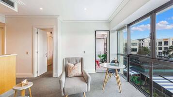 A modern hotel room with a balcony, a seating area with a small table, and a large window offering a city view.