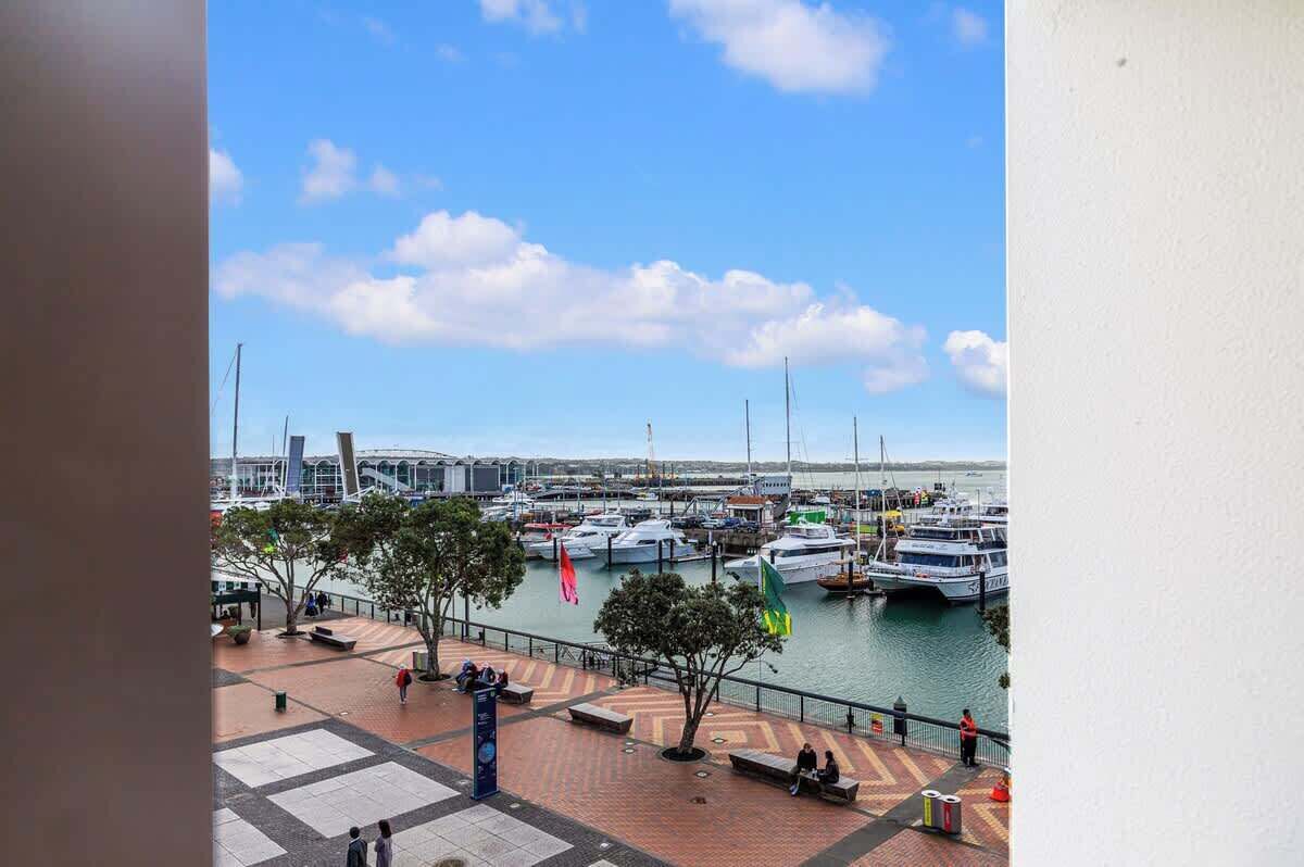 A marina with boats docked, a pedestrian walkway, and a clear sky.
