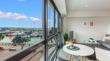 A modern room with a large window overlooking a marina, a round table with chairs, and a sofa.