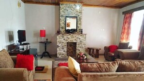 Una sala de estar con chimenea de piedra, sofás de cuero, un televisor y una pequeña mesa con una lámpara roja.