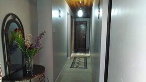 Un pasillo con un espejo, un jarrón con flores y una alfombra estampada que conduce a una puerta.