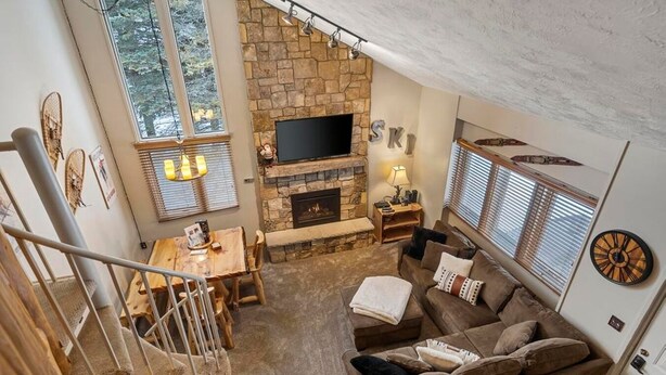 Una sala de estar acogedora con chimenea de piedra, un televisor de pantalla plana, un comedor con mesa y sillas, y una escalera que sube a un nivel superior.