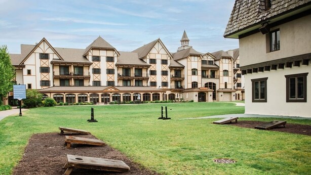 A large building with a symmetrical facade, multiple windows, and a central courtyard with a lawn and wooden benches. - Ramshead: Main Floor: Ski in Ski Out (Boyne Falls)