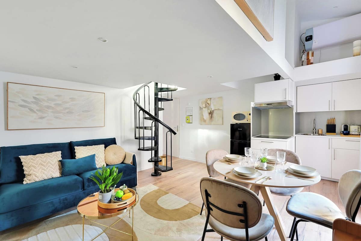 Ein modernes Wohnzimmer mit einem blauen Sofa, einem Essbereich mit einem runden Tisch und einer Wendeltreppe.