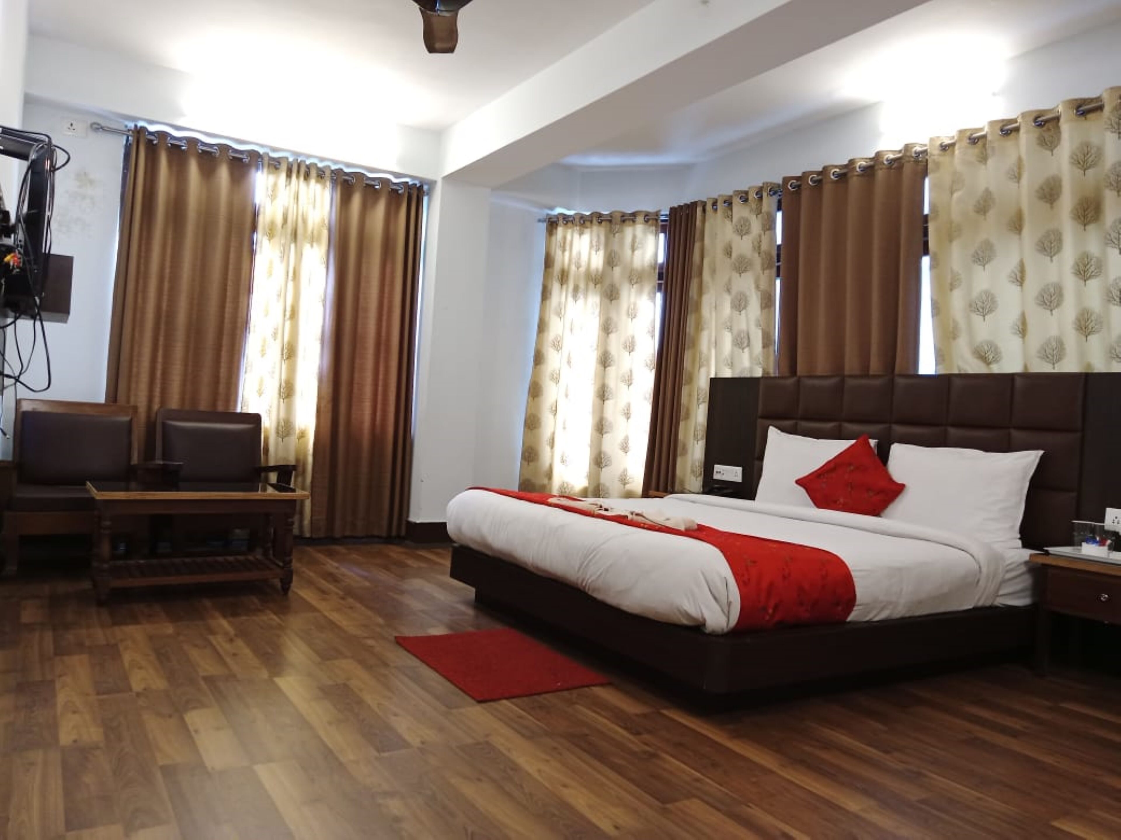 A hotel room with a large bed, a desk with a chair, a television, and curtains.