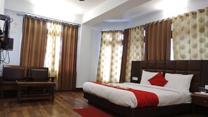 A hotel room with a large bed, a desk with a chair, a television, and curtains. - Hotel Dew Pond  (Gangtok)