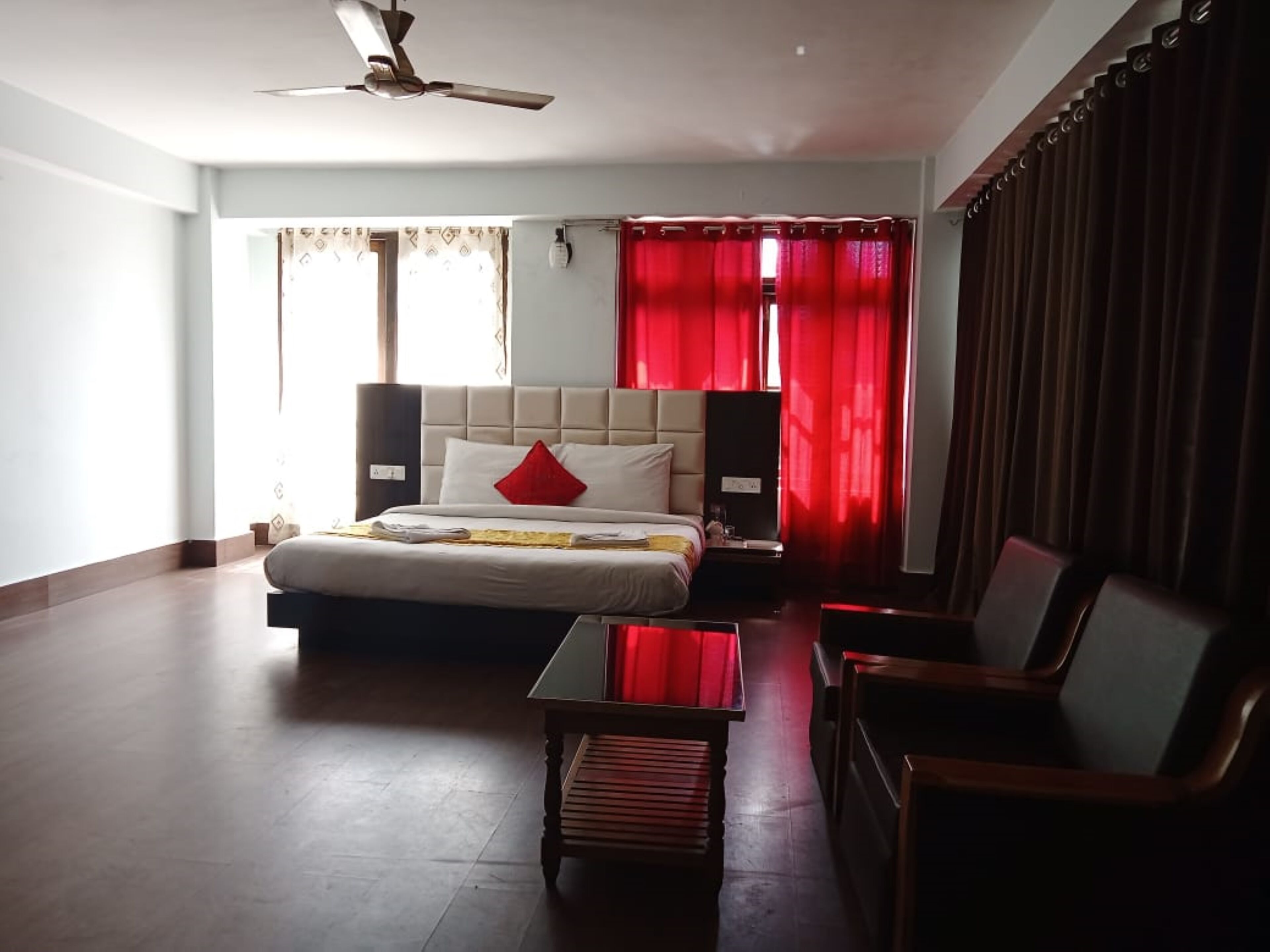 Une chambre d’hôtel avec un lit, un bureau, une chaise, un ventilateur de plafond et des rideaux rouges.