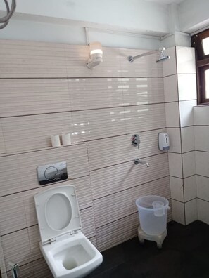 Ein Badezimmer mit Toilette, Handtrockner, Seifenspender und Duschkopf.